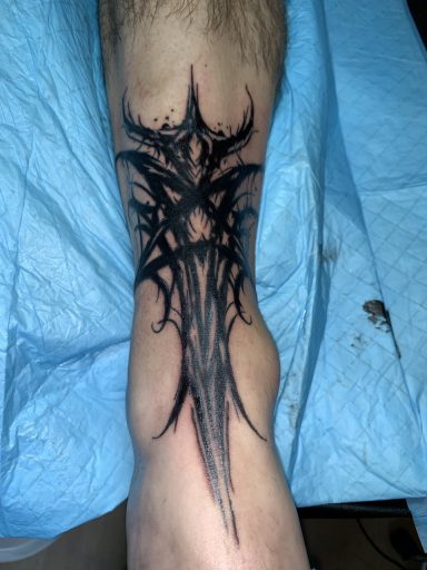 Schwarzes, kompliziertes Tattoo in Form von Bögen und Spitzen auf dem Unterarm.