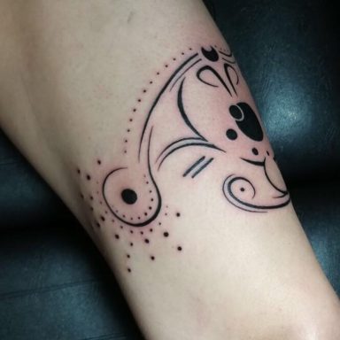 Schwarzes, dekoratives Tattoo mit geschwungenen Linien und Punkten am Oberschenkel.