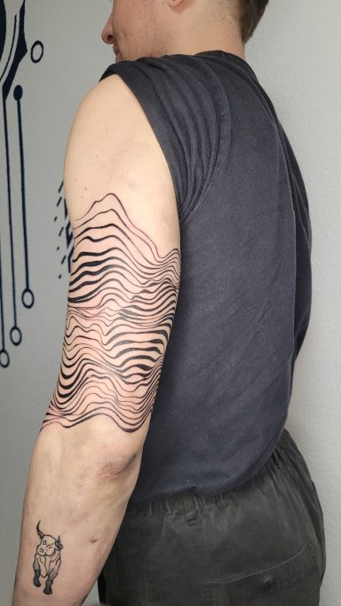 Männlicher Arm mit einem Wellenmuster-Tattoo und kurzem Ärmelschnitt des Oberteils.