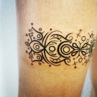 Schwarzes, dekoratives Tattoo mit symmetrischen Mustern auf einem Oberschenkel.