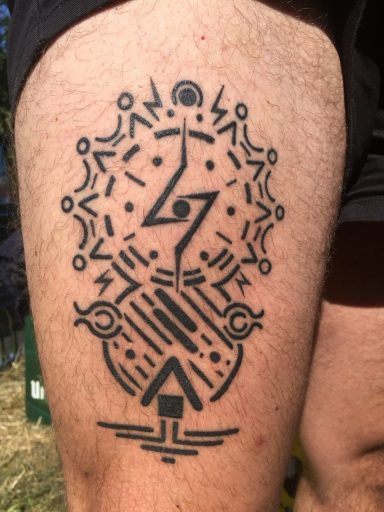 Schwarz-weißes Tattoo mit geometrischen Mustern und symbolischen Figuren auf einem Oberschenkel.