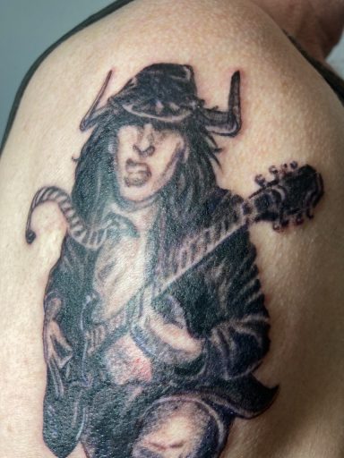 Tattoo eines spielenden Musikers in einem Hut, der eine Gitarre hält.