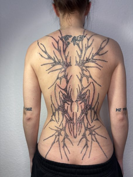 Rückenansicht einer Person mit komplexem, schwarzen Tattoo-Muster.