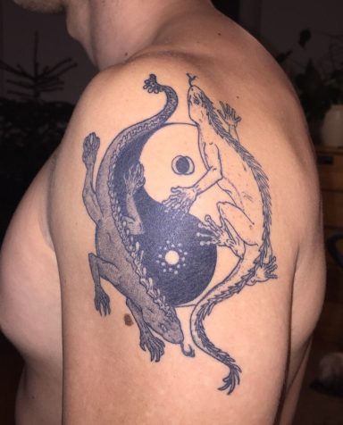 Tätowierung auf dem Oberarm mit Yin-Yang-Symbol und mythologischen Figuren.