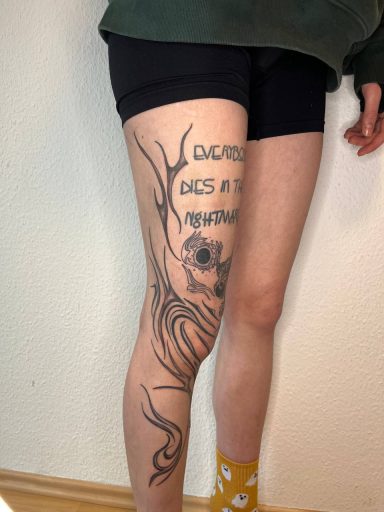 Ein Bein mit einem kunstvollen Tattoo, das einen Text und stilisierte Elemente zeigt.