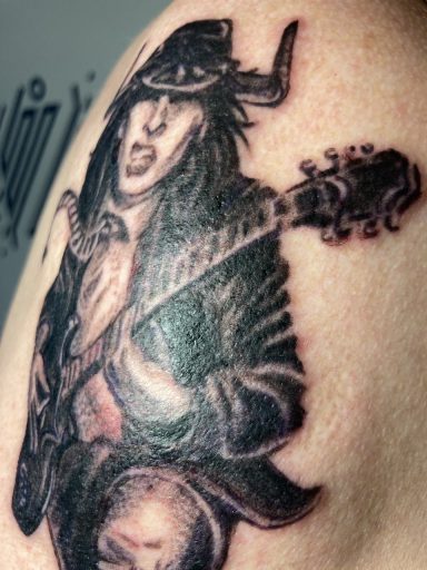 Tattoo eines spielenden Musikers in einem Hut, der eine Gitarre hält.