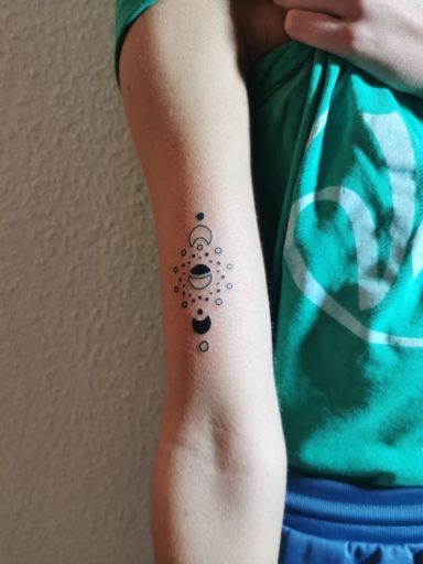 Schwarzes Tattoo mit Mondphasen und geometrischen Mustern auf einem Arm.