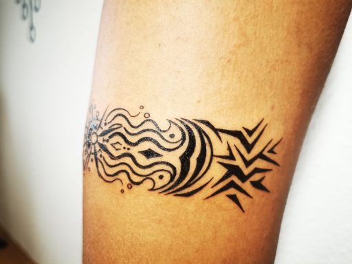 Schwarzes Tattoo mit geschwungenen Linien und geometrischen Formen auf einem Unterarm.