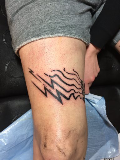 Schwarz-weißes Tattoo auf dem Oberschenkel mit Wellen- und Blitzmustern.