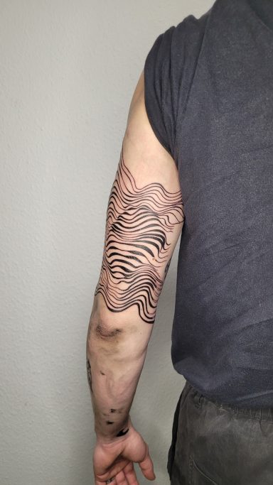 Tattoo auf einem Oberarm, zeigt eine abstrakte Wellen- und Linienstruktur.