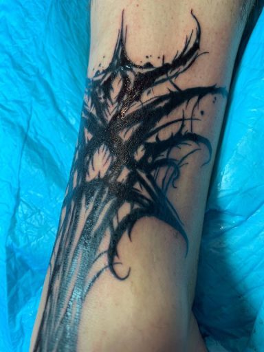 Schwarzes, abstraktes Tattoo auf dem Unterarm mit spitzen, verzweigten Formen.