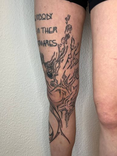 Tattoo auf dem Oberschenkel, zeigt abstrakte Muster und Schriftzüge.