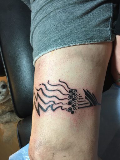 Schwarzes Tattoo auf dem Unterarm mit wellenförmigen Linien und Punkten.