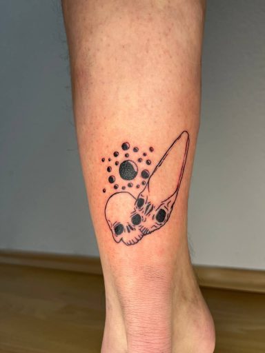 Tattoo eines Schädels mit einem Kometen und schwarzen Punkten auf einem Unterarm.