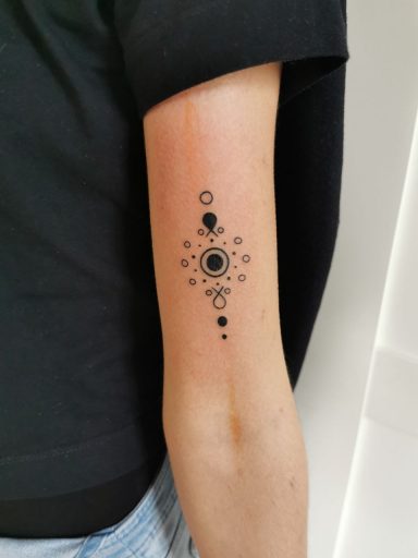 Schwarzes Tattoo auf dem Unterarm mit geometrischen Mustern und Kreisen.